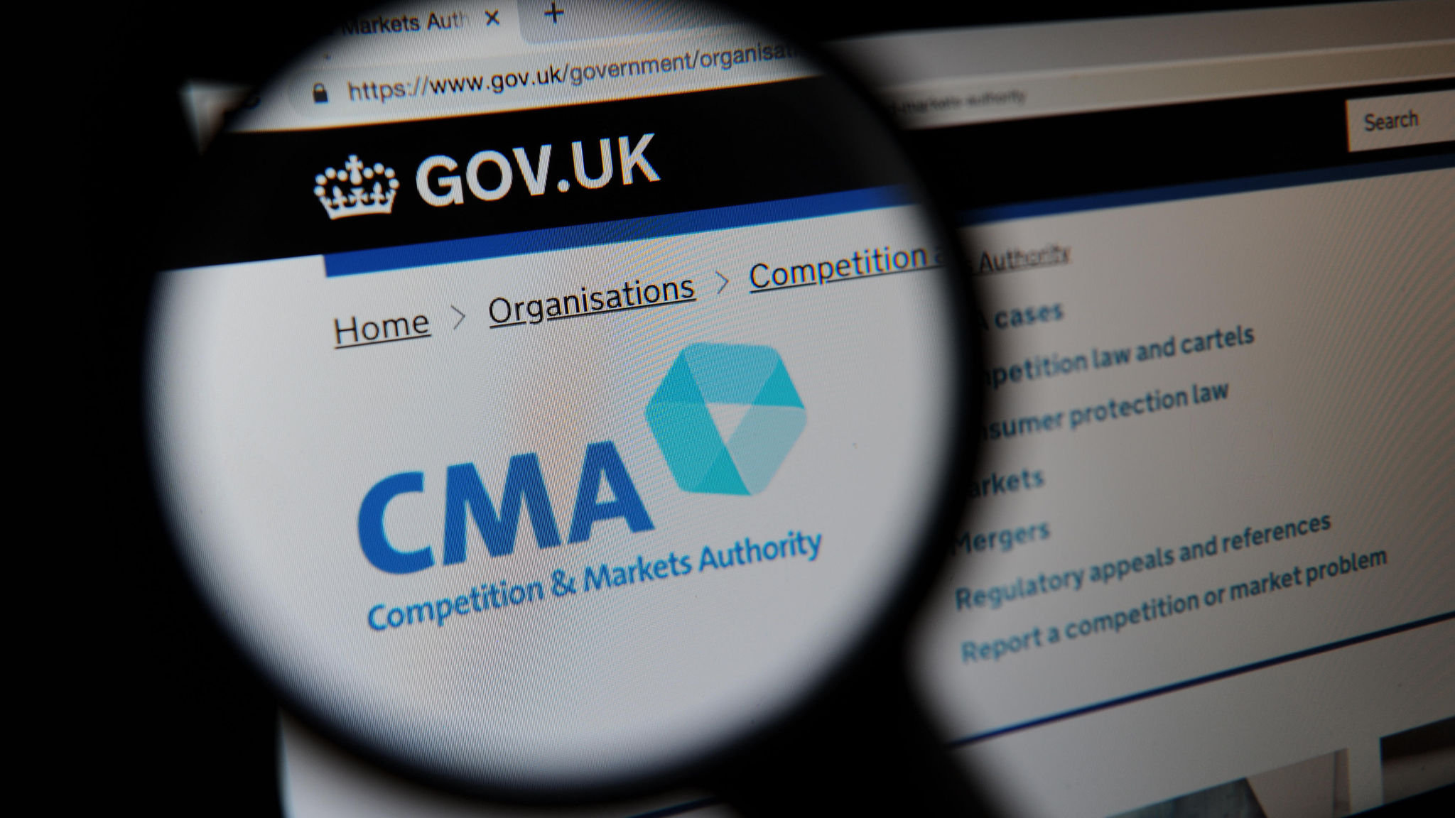 The Competition and Markets Authority (CMA) website seen through a magnifying glass